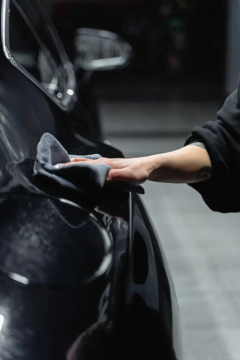 Gloved hand wiping a black car panel with a microfiber towel