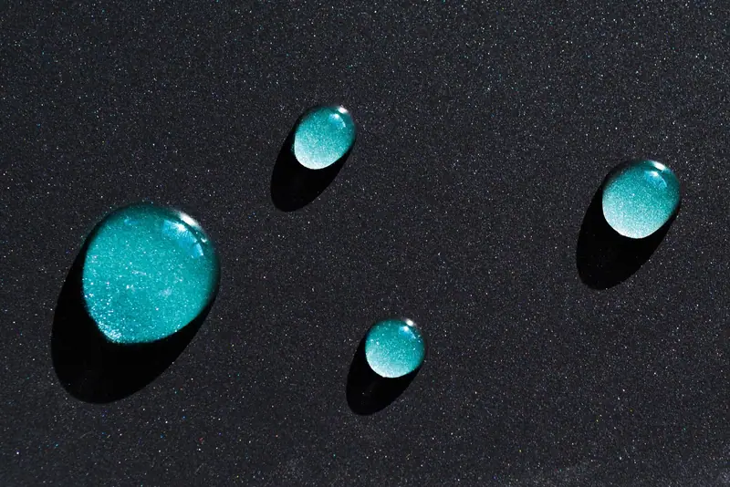 Four water beads sitting on glossy black paint