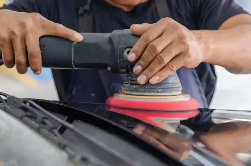 Machine polisher working a black car hood