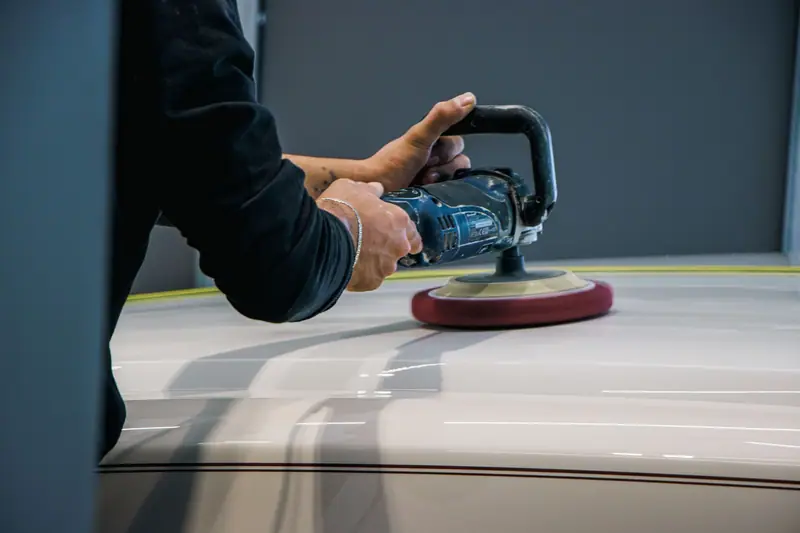 Red polishing pad buffing a gray car panel