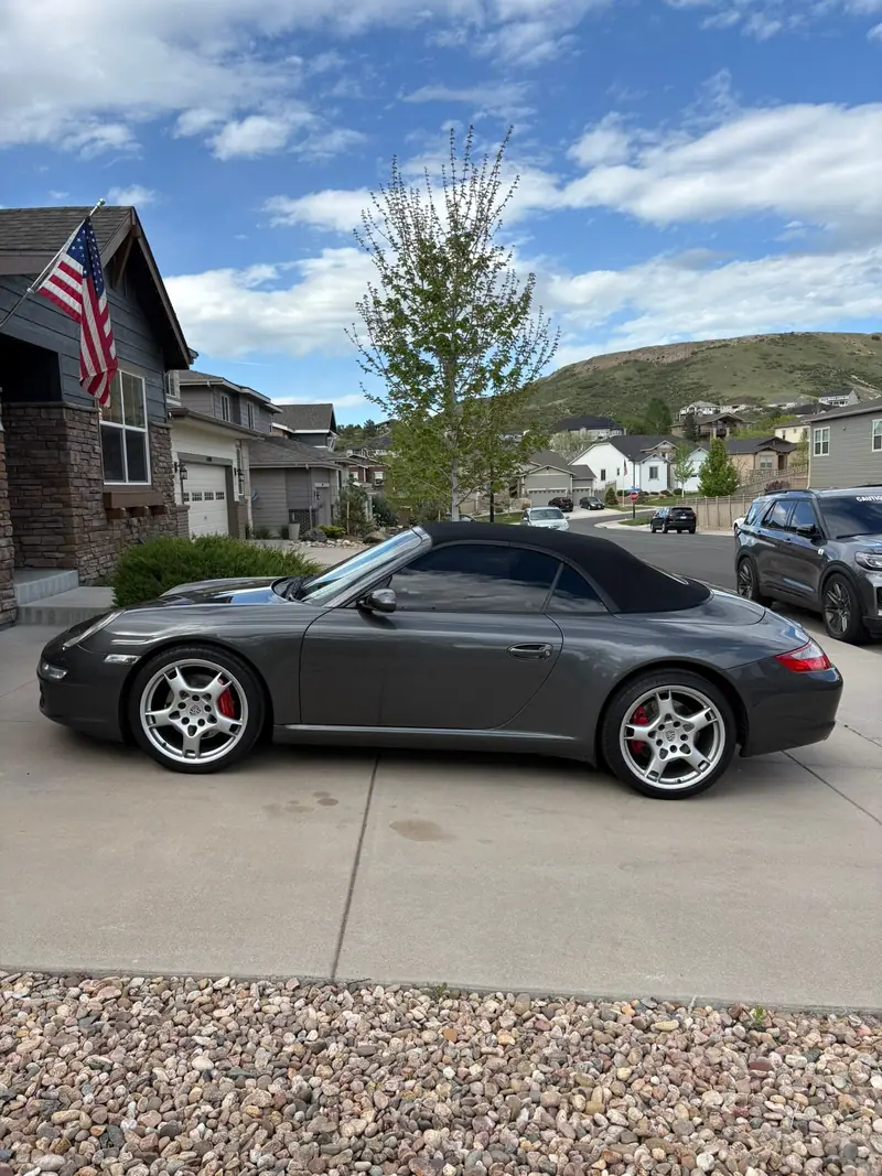 Gray Porsche 911 convertible by a home flying an American flag