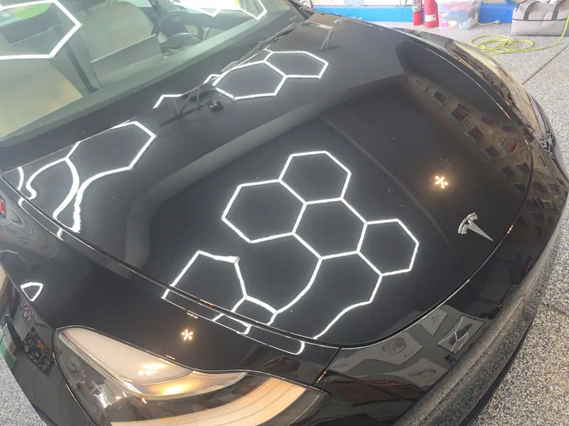 Black Tesla hood mirroring hexagon shop lights after ceramic coating