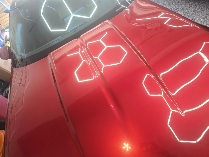 Red Corvette hood reflecting hexagon garage lights in deep gloss