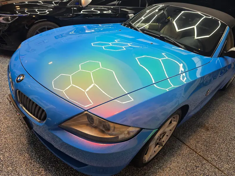 Blue BMW Z4 hood with corrected paint mirroring hexagon shop lights