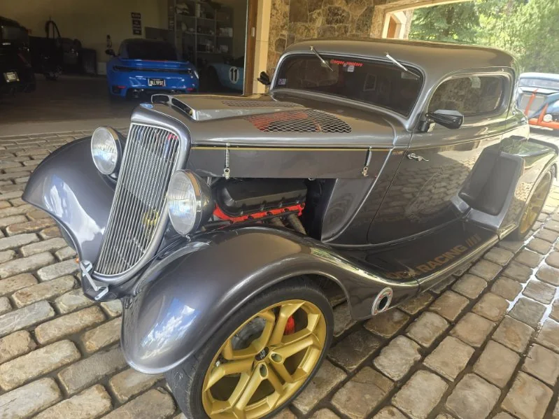 Gray 1930s Ford coupe hot rod with gold wheels on a stone driveway, paint glossy after detailing