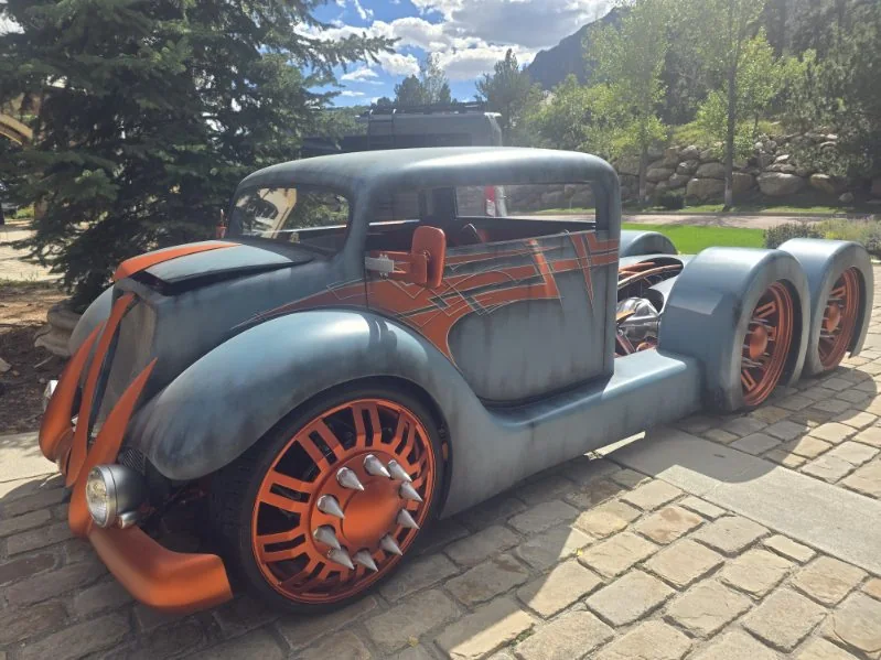Blue patina rat rod with orange pinstriping and orange wheels in front of mountain trees