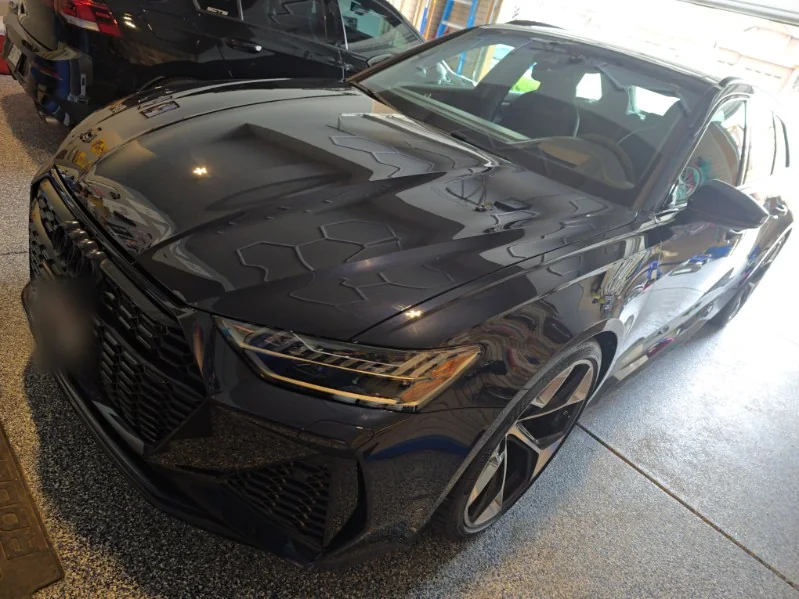 Dark Audi RS6 Avant front end reflecting hexagon garage lights